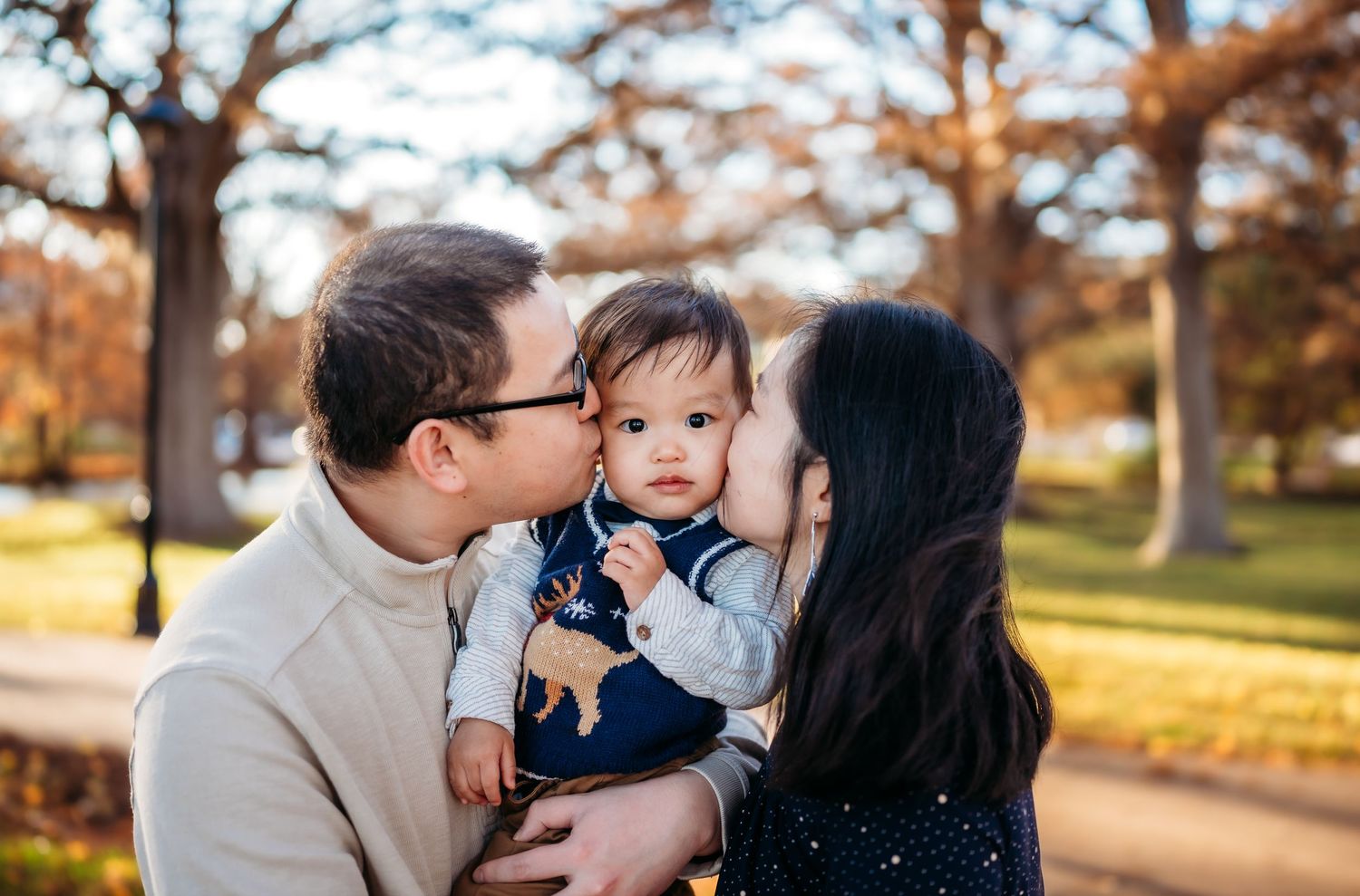 A loving family moment captured outdoors in a park during autumn with warm golden sunlight.