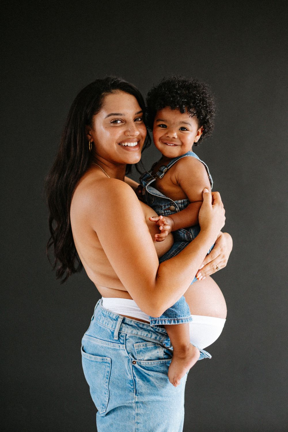 Parent and small child sharing joyful moment together against dark background in casual attire.