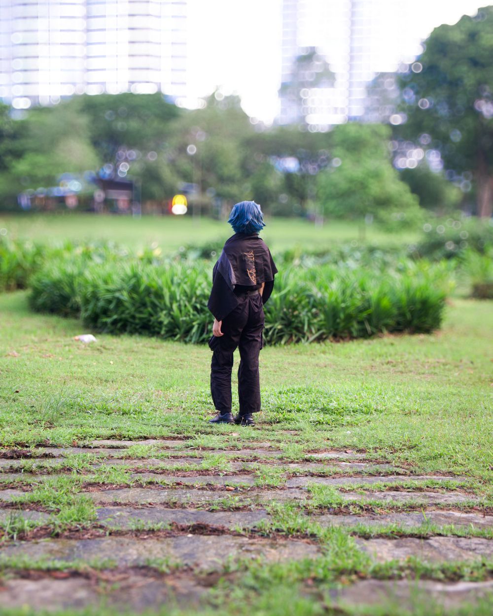 A silhouetted figure stands alone in a grassy park with buildings in the background.