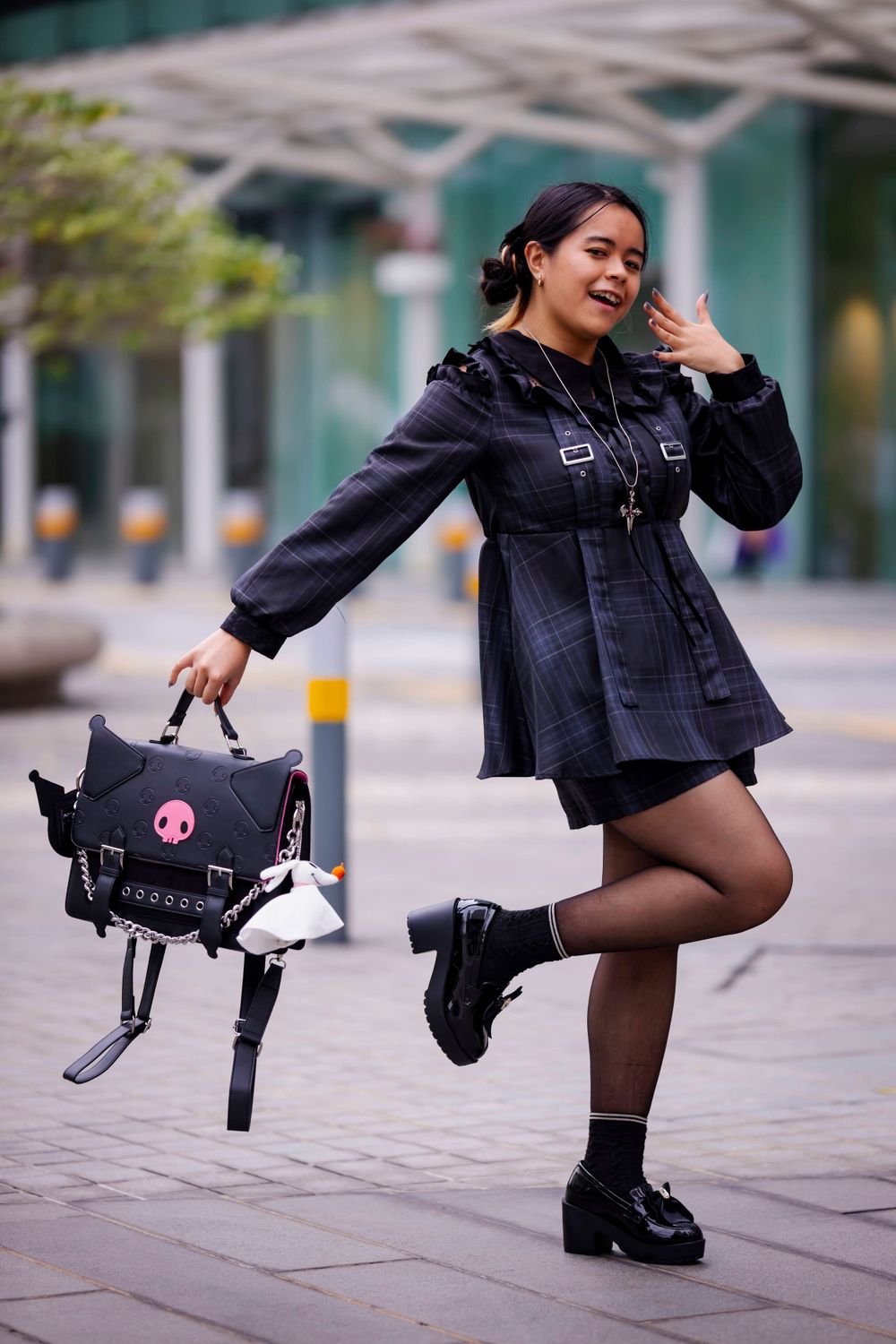 A person in a dark dress holding a decorative bag poses playfully on a city street.