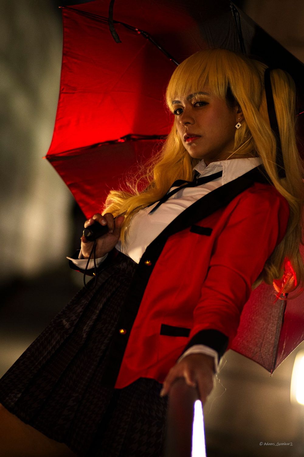Cosplay character in red jacket and plaid skirt poses with red umbrella in dramatic lighting.