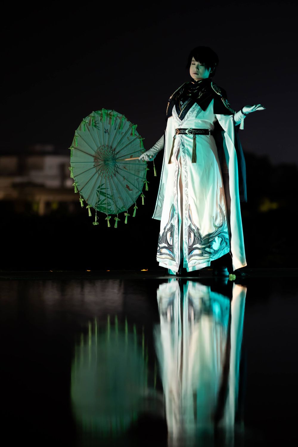 Costumed performer with ornate parasol creates dramatic reflection in water at night.