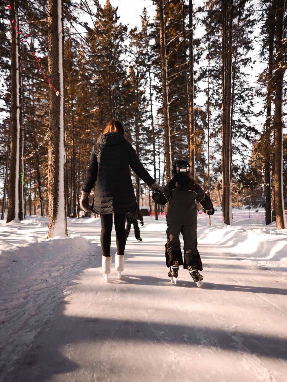 People ice skating together on a snowy forest path during winter.