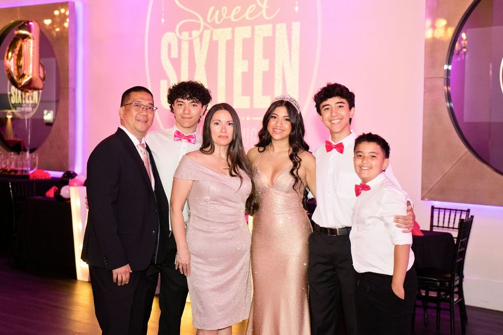 Family of six posing together at a Sweet Sixteen birthday celebration in an elegant decorated venue.