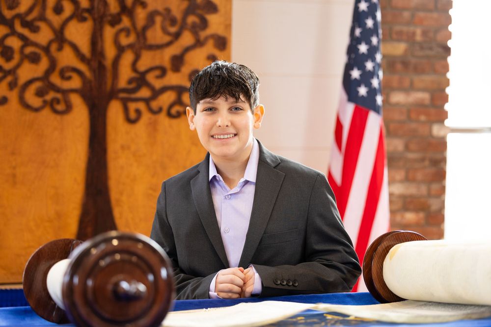 Young boy in a blazer sits proudly at the Torah table during his Bar Mitzvah ceremony.