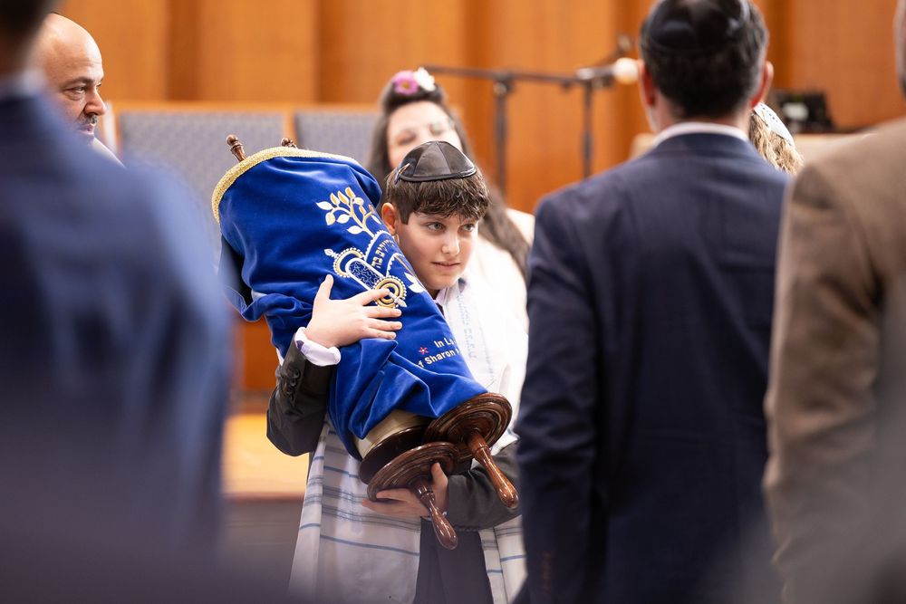 Young boy carrying a Torah scroll wrapped in blue velvet cover during a Jewish synagogue service.