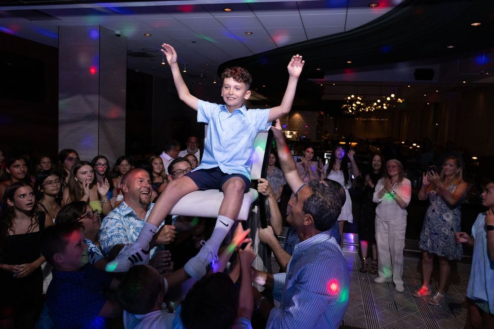 Young boy lifted by crowd with arms raised during a joyful Bar Mitzvah party.