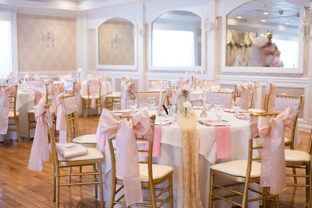 Elegant banquet hall with gold chiavari chairs and pink sash decorations for an event.