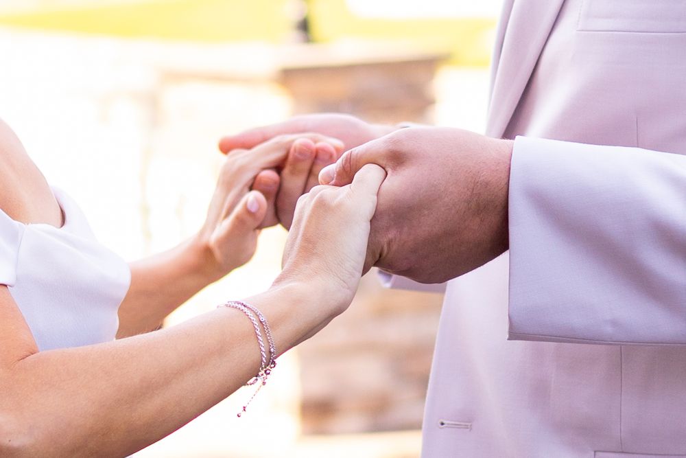 Close-up of bride placing wedding ring on grooms finger during outdoor wedding ceremony exchange.
