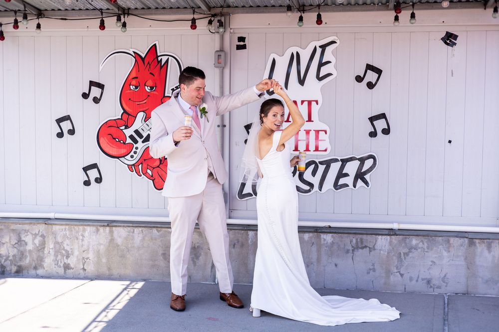 Bride and groom dance playfully in front of colorful Live at the Lobster mural on their wedding day.
