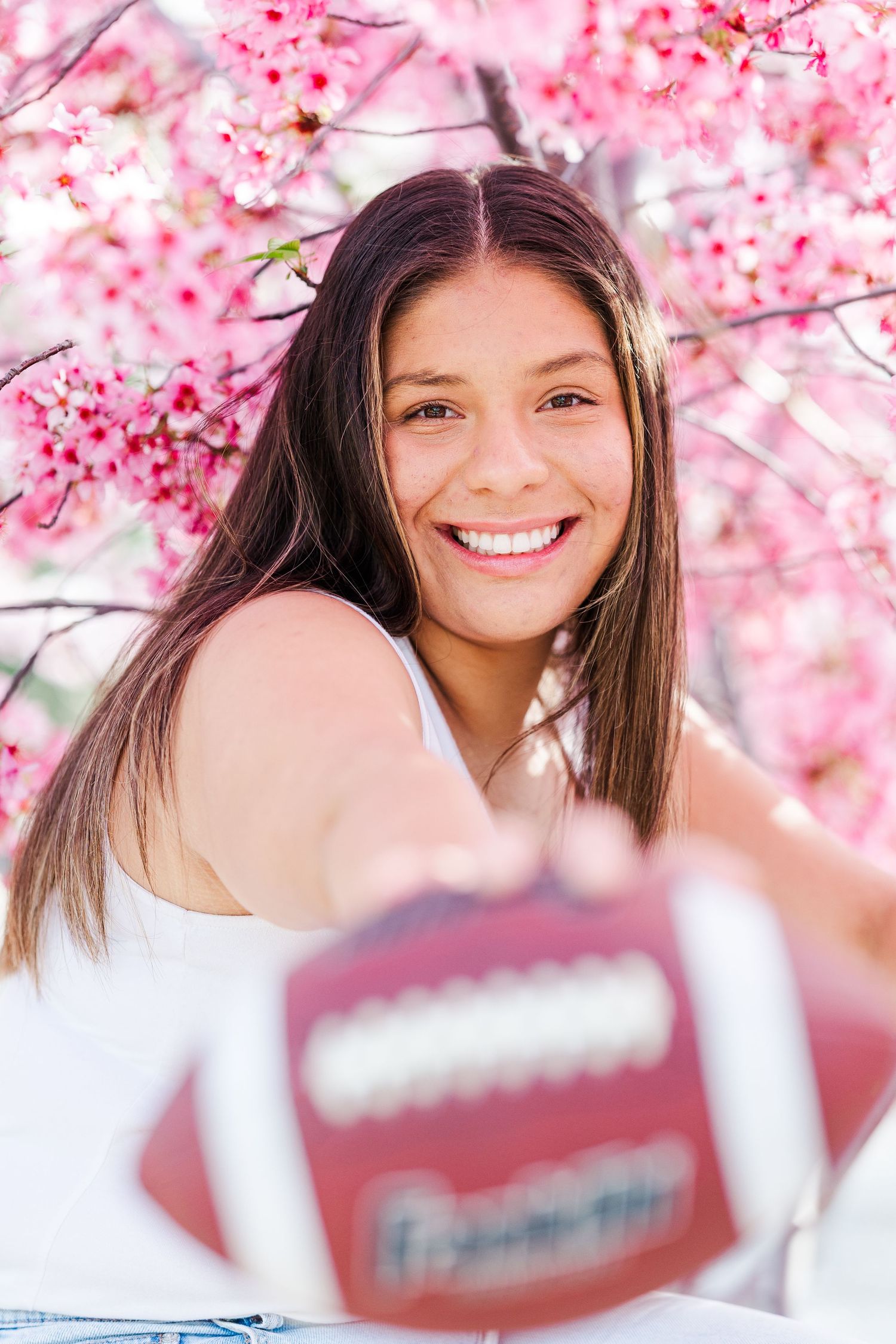 A smiling person poses with a football beneath blooming pink cherry blossoms on a bright spring day in Simi Valley, CA