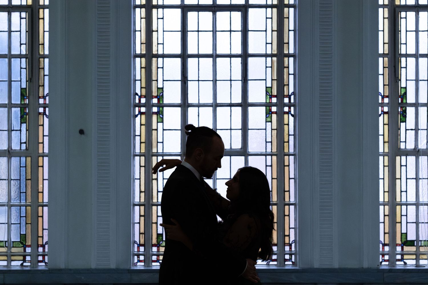 Silhouette of a dancing couple in front of tall windows with natural light streaming through the windowpanes.