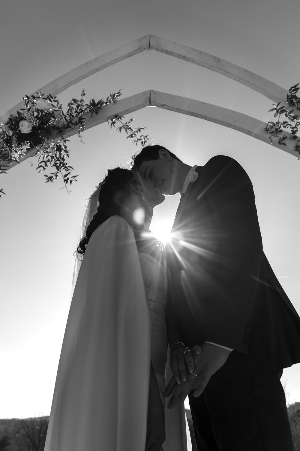 A romantic black and white wedding silhouette under an arch with sunlight bursting between the bride and groom.