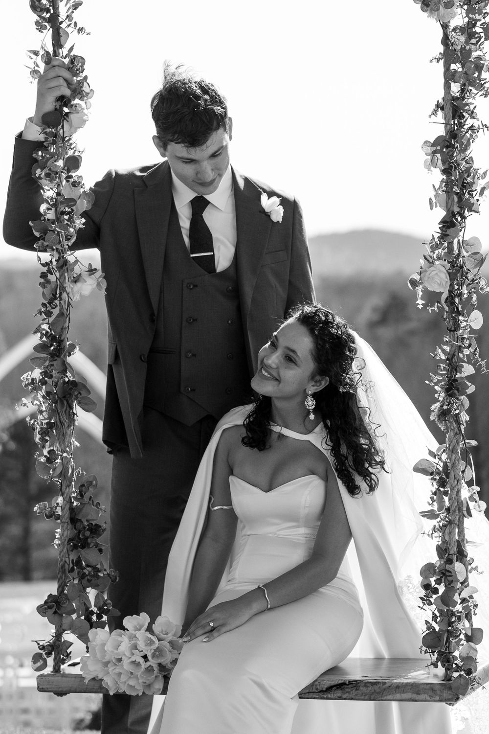 Newlyweds sharing romantic moment on decorative swing during wedding photoshoot.
