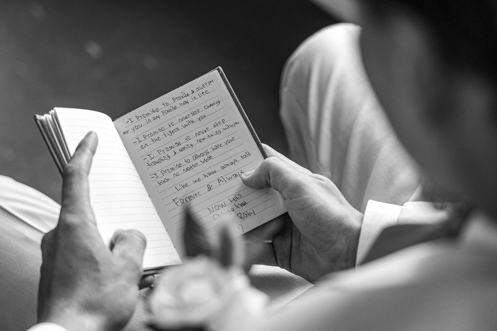Over the shoulder sneak peak of the groom reading his vow in monochromatic black and white style setting.