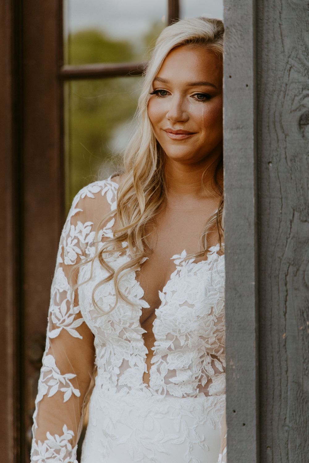 During the first touch, Bride wearing delicate lace long sleeve wedding gown posing by window listening to the groom reading his vows.