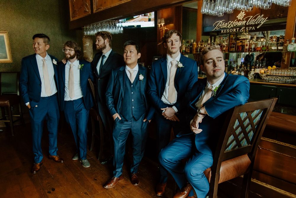 Groomsmen in navy blue suits posing together at wedding reception bar in a dramatic dark vibe / style.