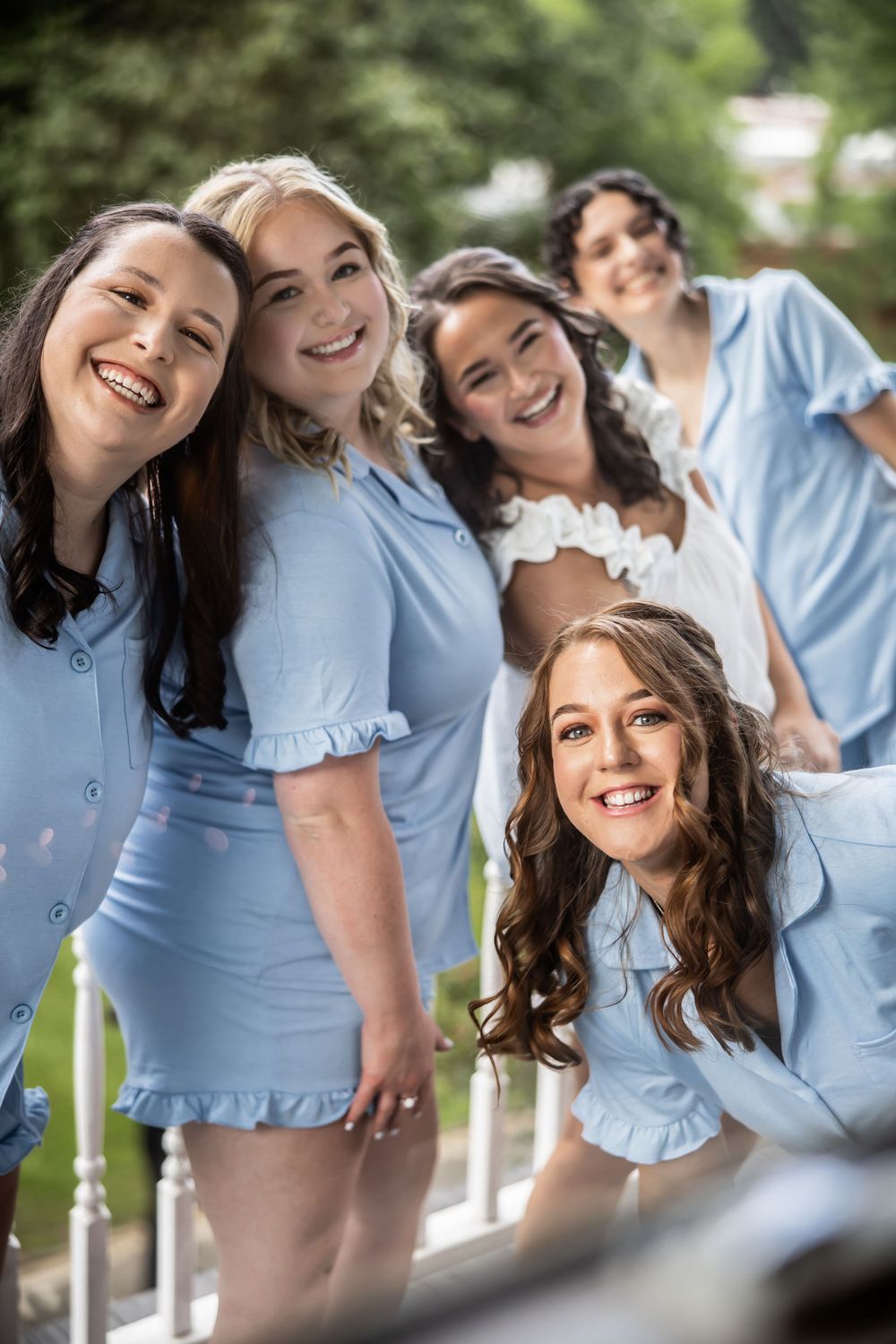 Group of bridemaids in matching light blue ruffled outfits pose together outdoors during a special occasion.