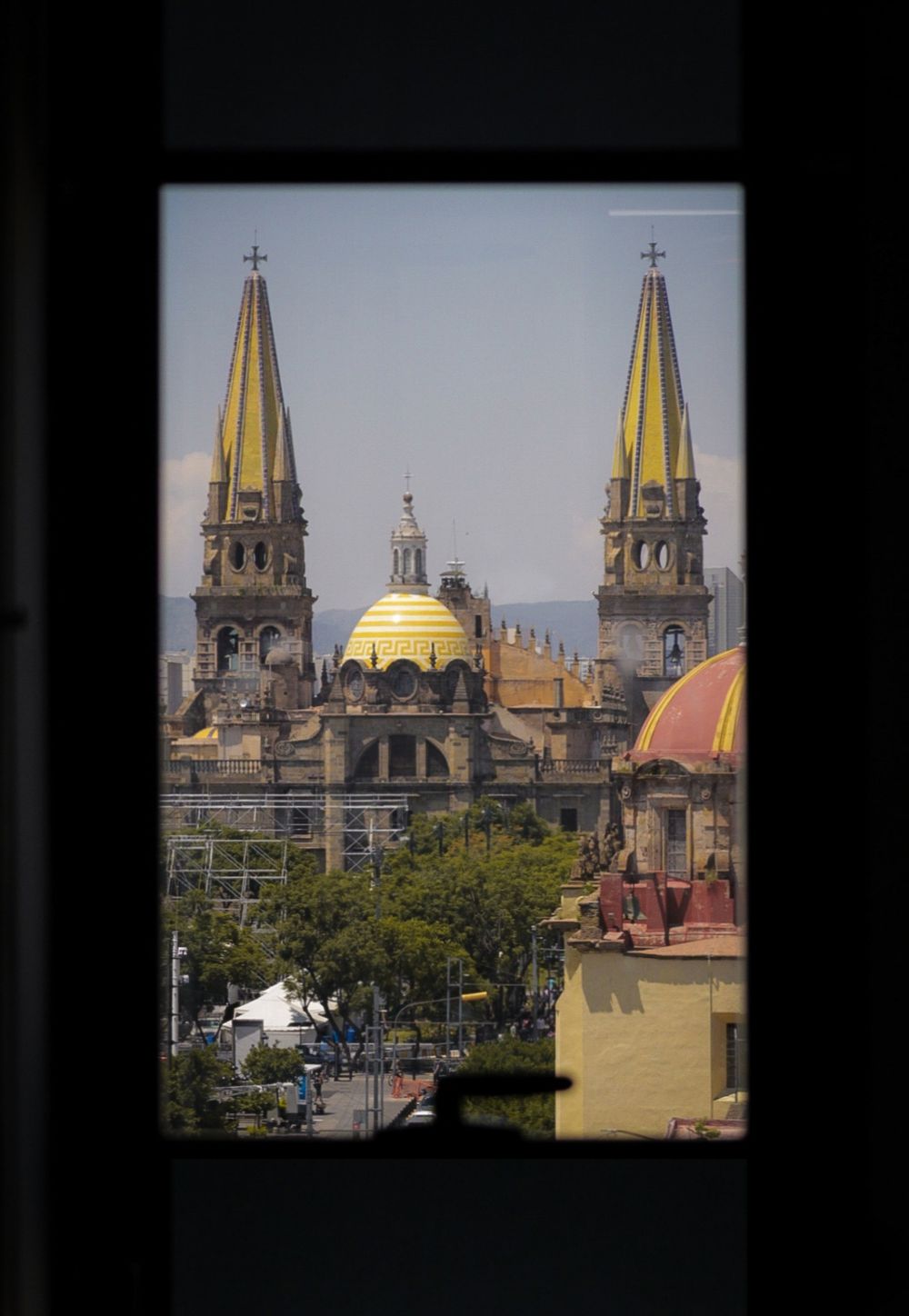 View of Guadalajara Cathedral with golden domes and twin towers framed through a dark window opening.