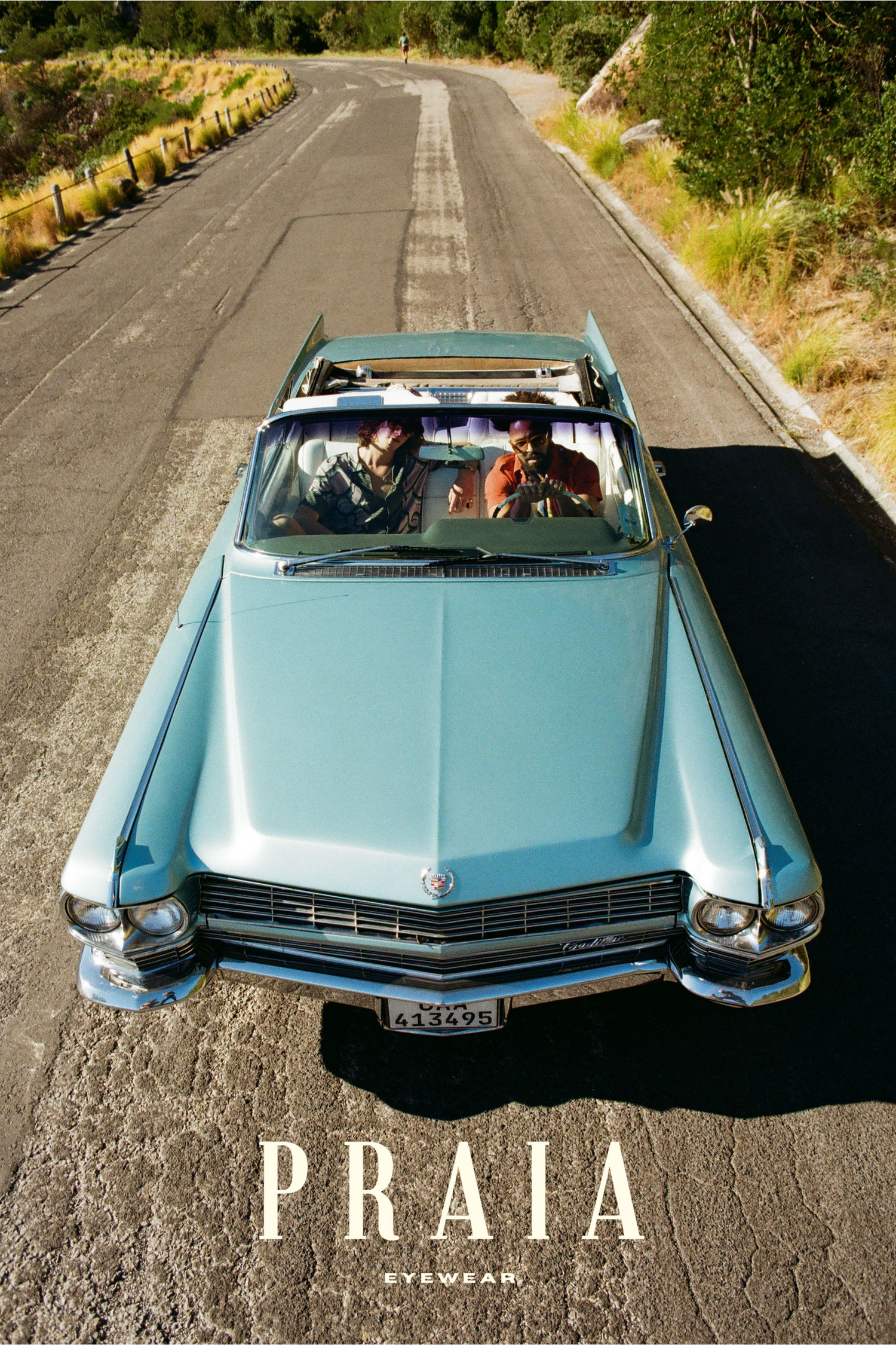 A vintage light blue Cadillac convertible drives down a sunny rural road in a retro summer scene with Praia text overlay.