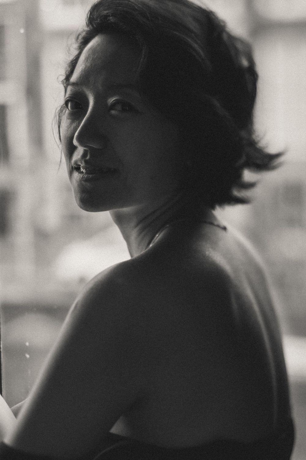 An artistic black and white portrait of a person in moody window light.