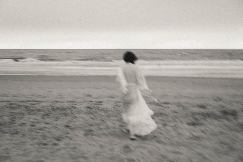 Person in white dress walking along empty beach horizon.