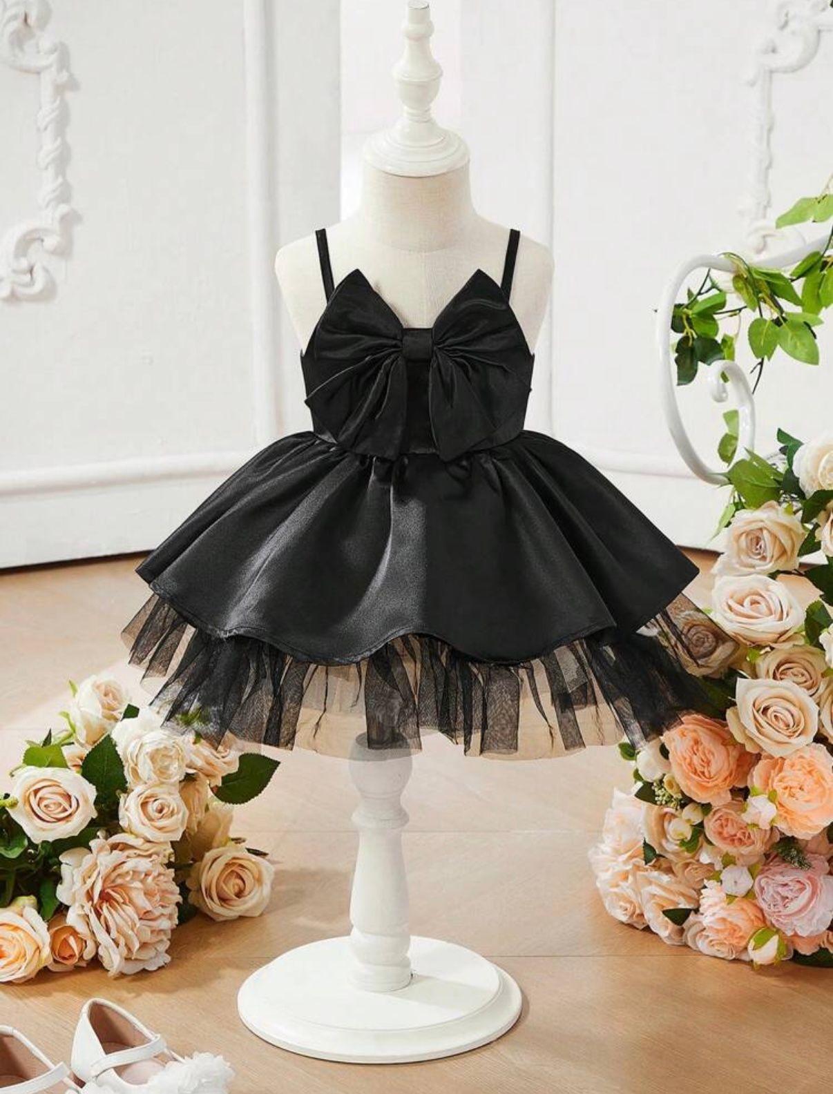 Black tutu dress with bow detail displayed on mannequin surrounded by peach roses.