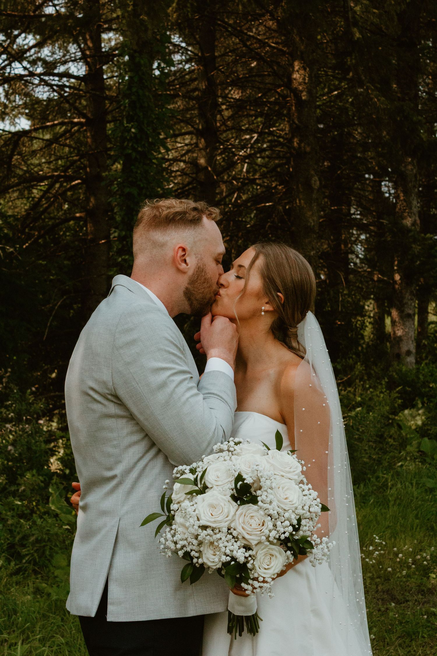 A romantic wedding moment captured in a forest setting with a white bridal bouquet and elegant attire.