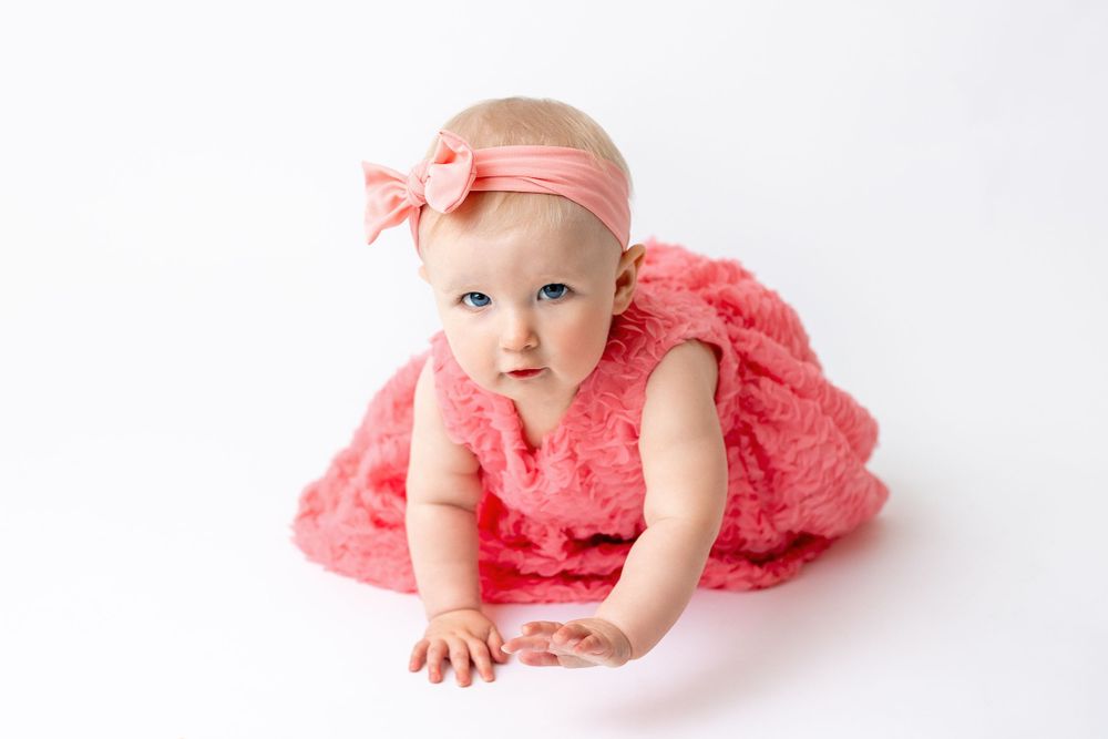 Cedar park TX photography milestone session, baby girl in white crib, coral pink dress and bow in her hair, studio White