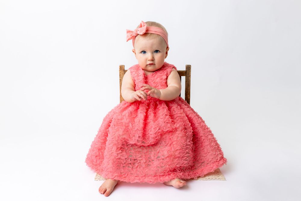 Cedar park TX photography milestone session, baby girl in white crib, coral pink dress and bow in her hair, studio White