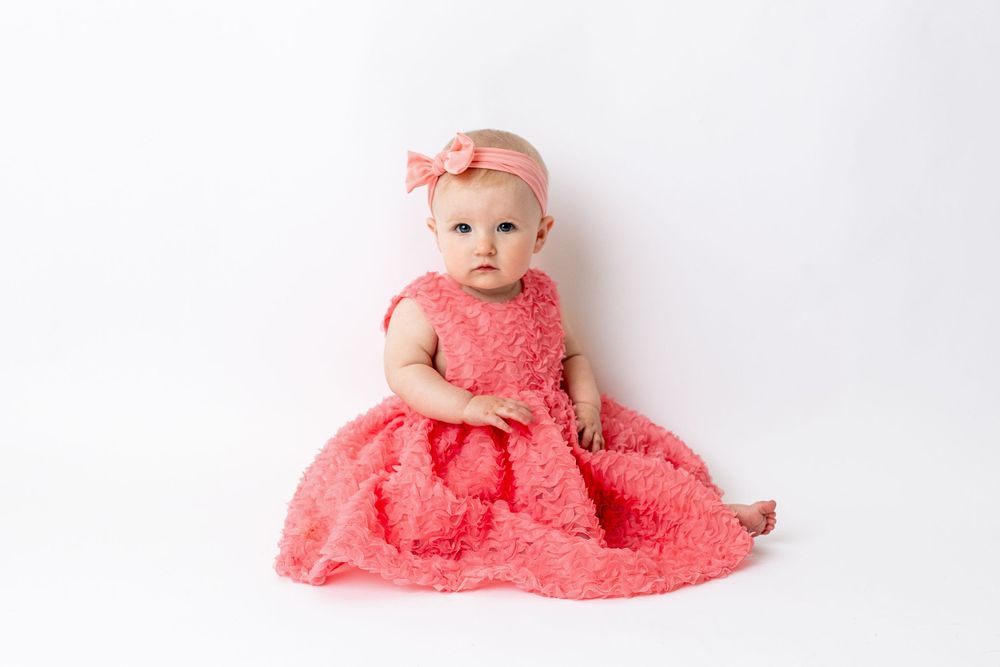 Cedar park TX photography milestone session, baby girl in white crib, coral pink dress and bow in her hair, studio White