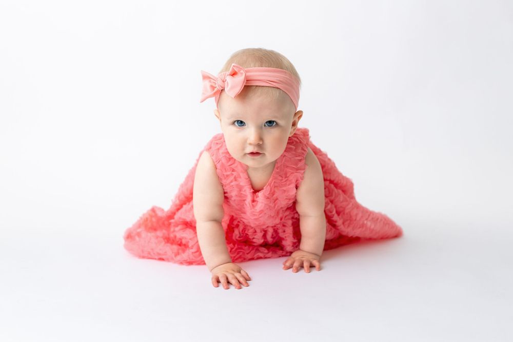 Cedar park TX photography milestone session, baby girl in white crib, coral pink dress and bow in her hair, studio White