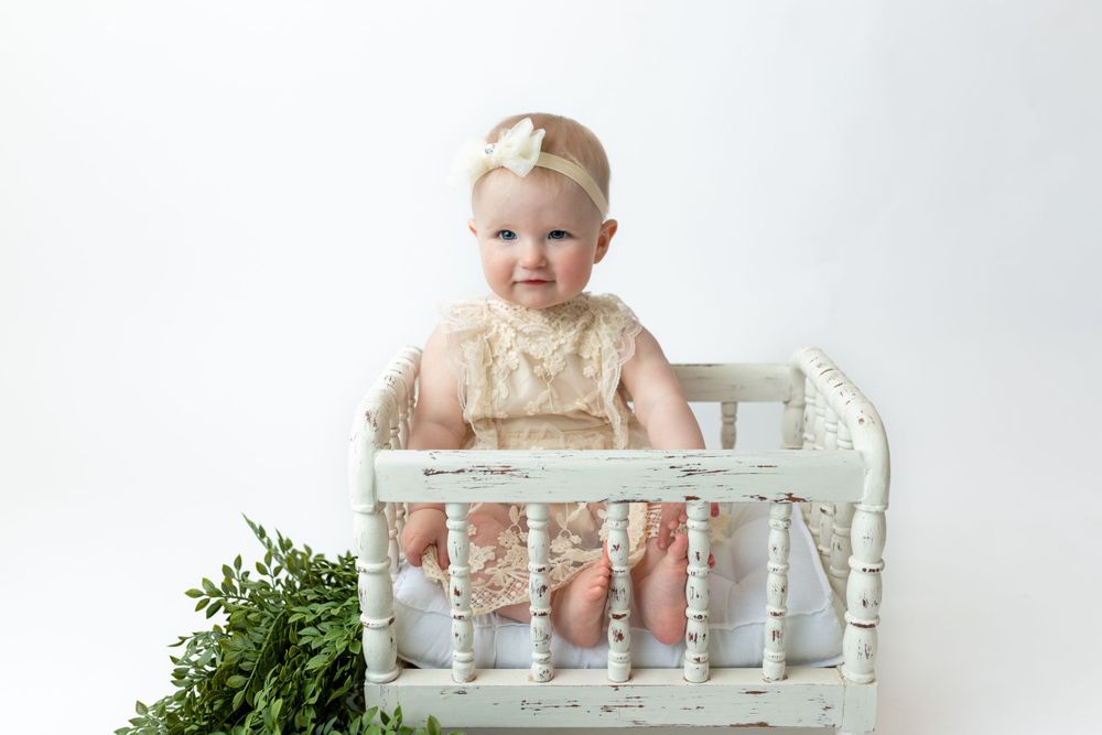 Cedar park TX photography milestone session, baby girl in white crib, lace cream dress and bow in her hair, studio white