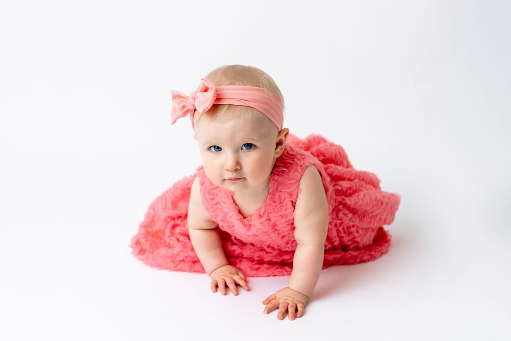 Cedar park TX photography milestone session, baby girl in white crib, coral pink dress and bow in her hair, studio White