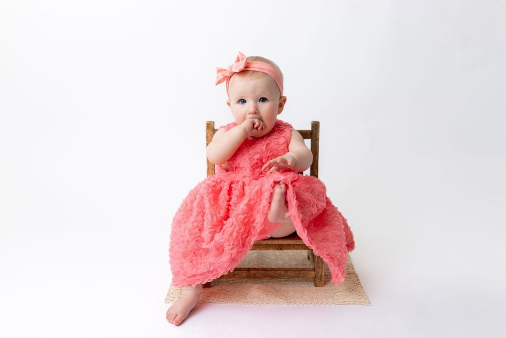 Cedar park TX photography milestone session, baby girl in white crib, coral pink dress and bow in her hair, studio White