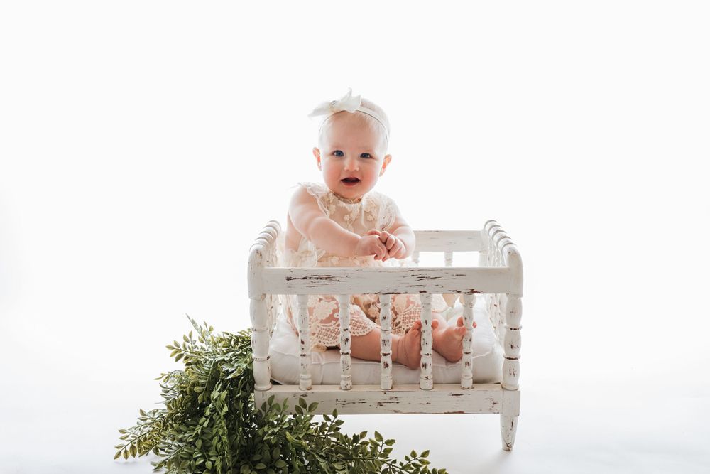 Cedar park TX photography milestone session, baby girl in white crib, lace cream dress and bow in her hair, backlit