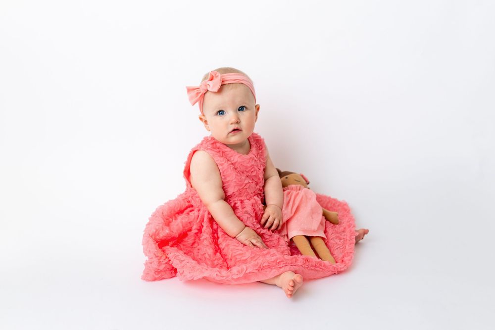 Cedar park TX photography milestone session, baby girl in white crib, coral pink dress and bow in her hair, studio White