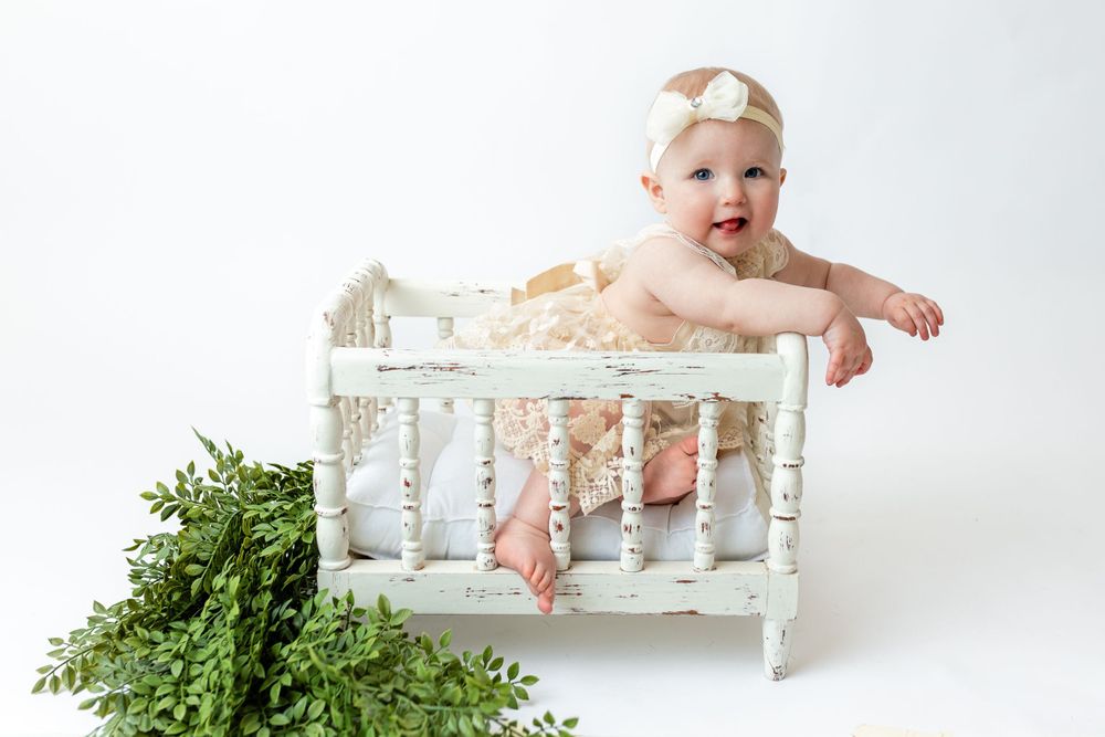 Cedar park TX photography milestone session, baby girl in white crib, lace cream dress and bow in her hair, studio white