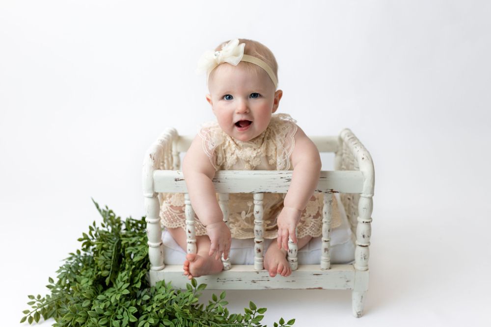 Cedar park TX photography milestone session, baby girl in white crib, lace cream dress and bow in her hair, studio white