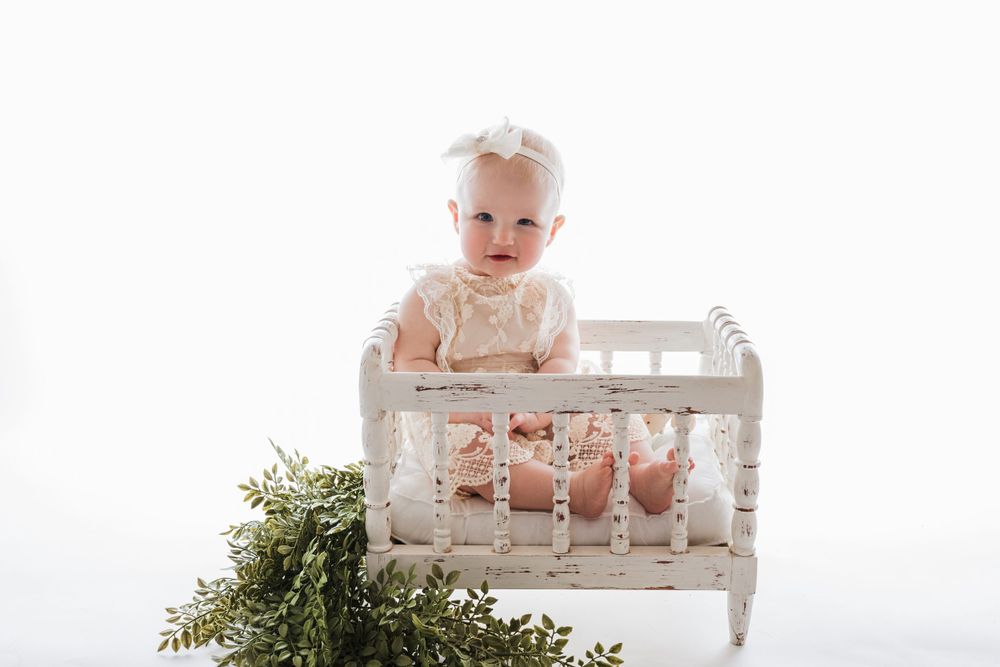 Cedar park TX photography milestone session, baby girl in white crib, lace cream dress and bow in her hair, backlit
