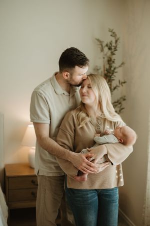A tender family moment at home as parents hold their newborn baby while standing next to a potted plant.