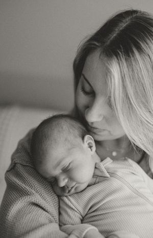 A tender black and white portrait of a mother holding her sleeping newborn baby against her chest.
