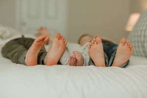 Three pairs of bare feet lined up on a white bed, showing a sweet family moment of relaxation together.