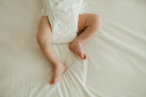 Small baby legs wearing a white diaper rest on soft white bedding.
