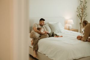 A cozy bedroom scene with a person relaxing on white bedding while looking at a mobile phone.