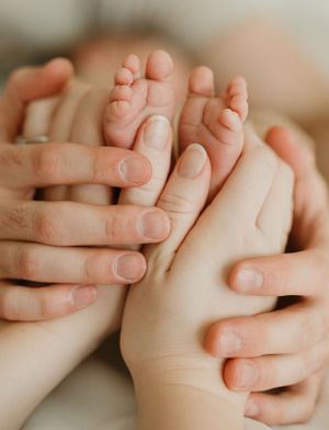 Close-up of gentle hands cradling tiny newborn baby feet with soft natural lighting.