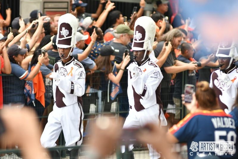 Marching band members in white uniforms performing synchronized moves during a performance.