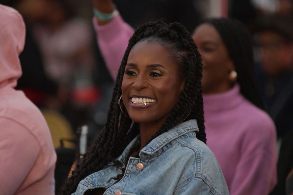 A person wearing a denim jacket smiles warmly at an outdoor event.
