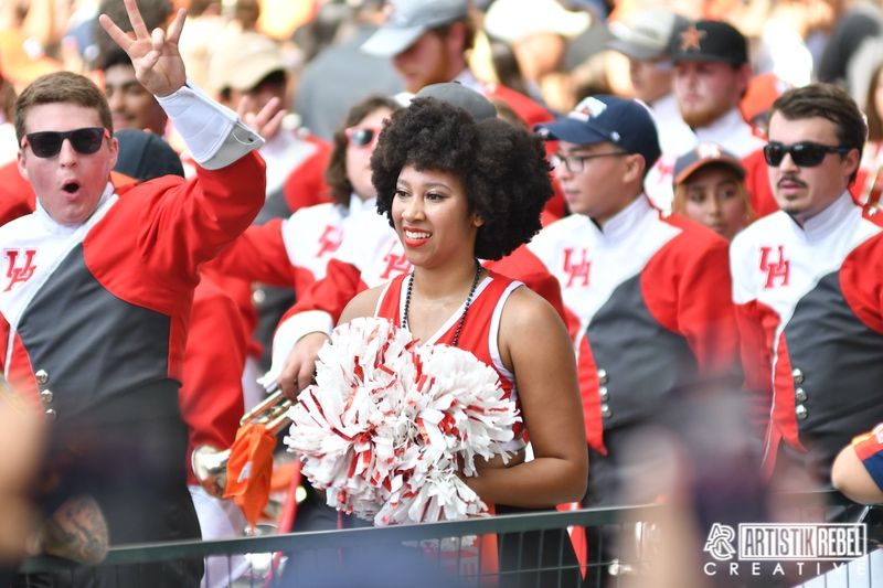 Cheerleader in red and white uniform performing with crowd in background.