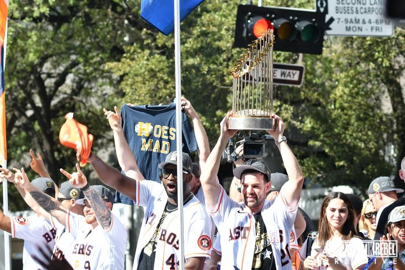 Baseball players raise championship trophy while riding on parade float through city streets.